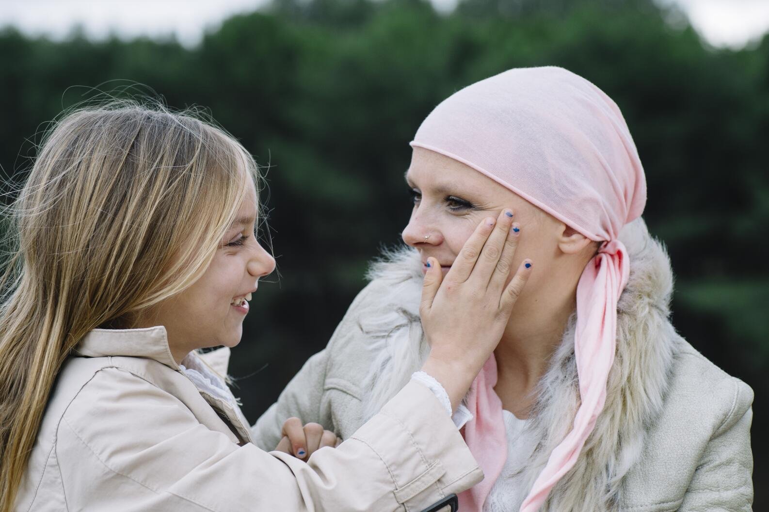A woman with cancer is next to her daughter. A girl is hugging a woman happy