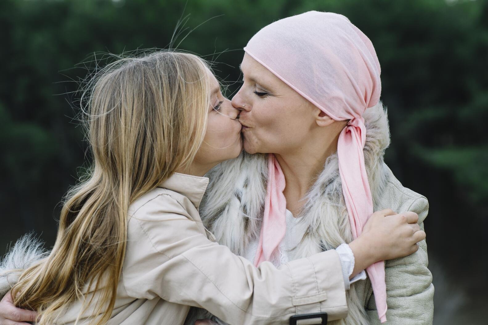 A woman with cancer is next to her daughter. A girl is hugging a woman happy