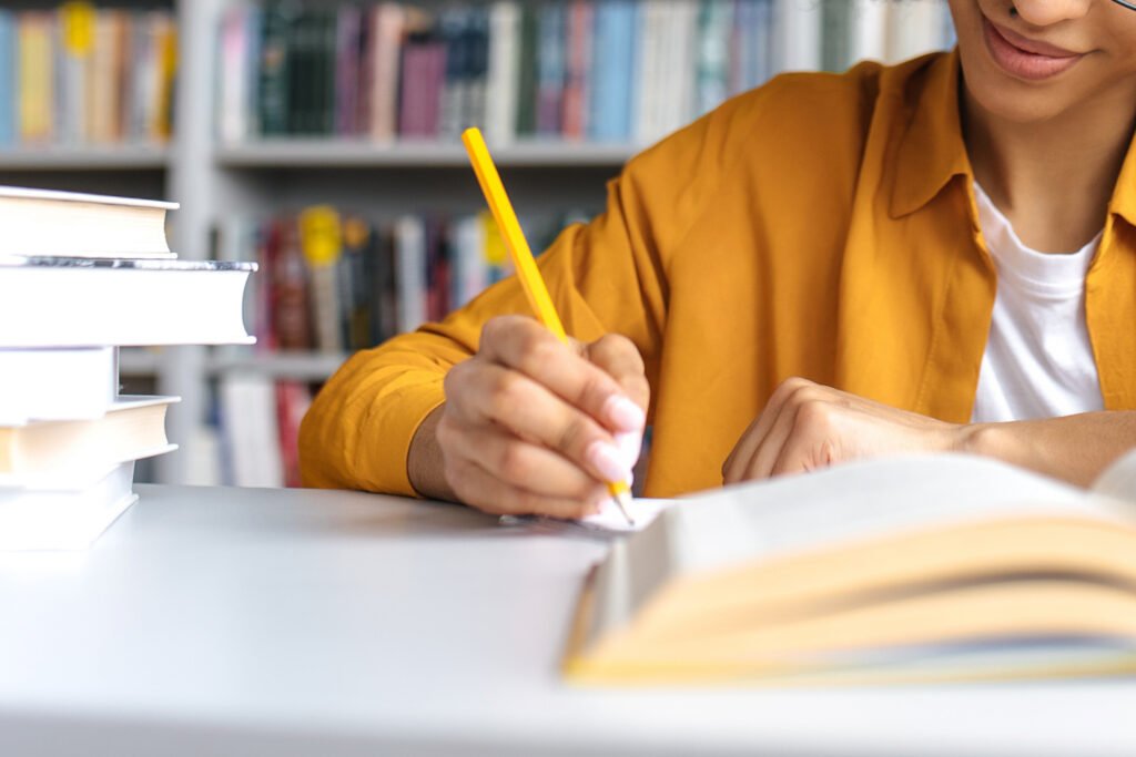 Teenage african american female student studying while sits at the table in the college library, reads books to searching information for a lesson or exam, doing homework and notes, gaining knowledge
